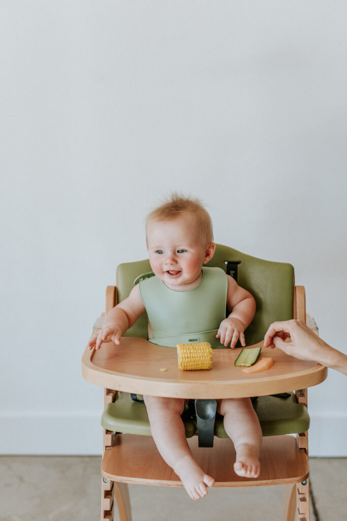 hayes in high chair with corn and vegetables laughing